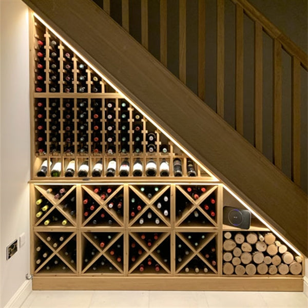 Wine bottles arranged in a wooden wine rack placed under stairs.