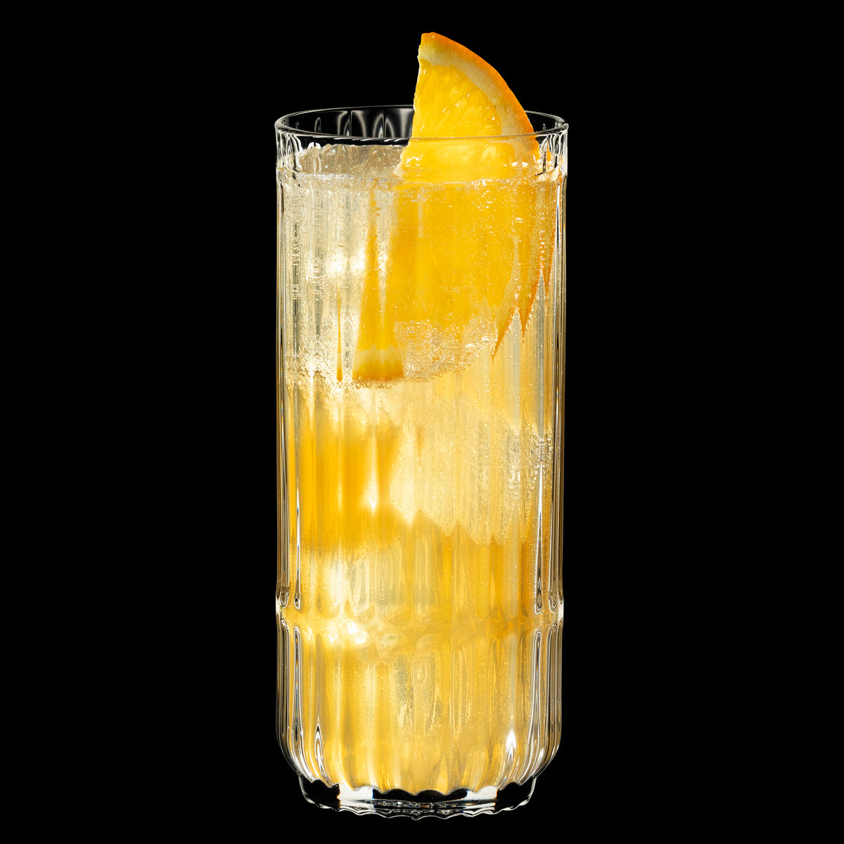 A tall, clear Riedel Restaurant Bar Rituals Highball Tumbler (321ml) from the 0421/04 set is filled with a fizzy, light-colored beverage, ice cubes, and garnished with an orange slice. Crafted from lead-free crystal by Riedel and sold as a set of 12, the glass stands out against a solid black background.
