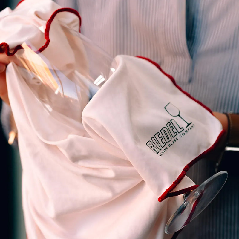 Person cleaning a wine glass with a branded Riedel cleaning cloth.