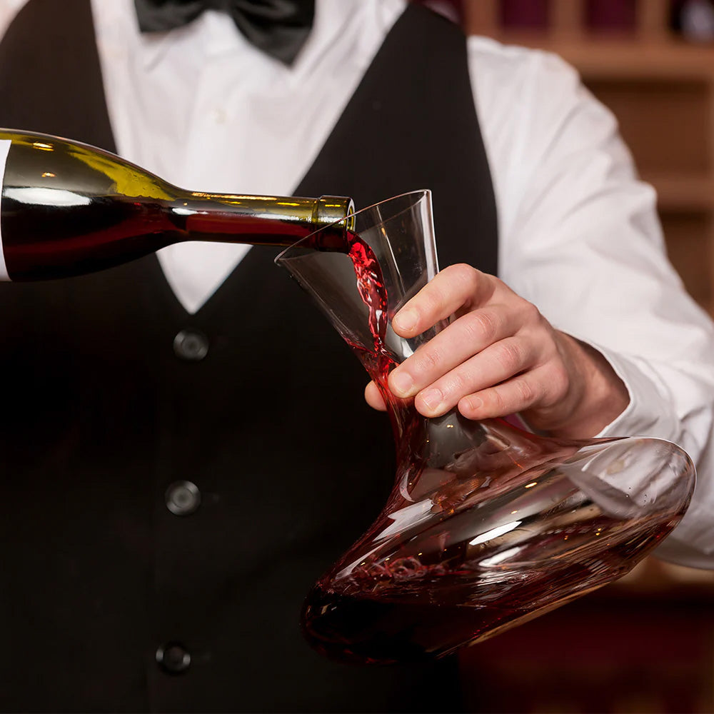 A person in formal attire pours red wine into a Stölzle Classic Mouth-Blown Red Wine Decanter 750ml, carefully holding the handmade crystal decanter to aerate the wine.