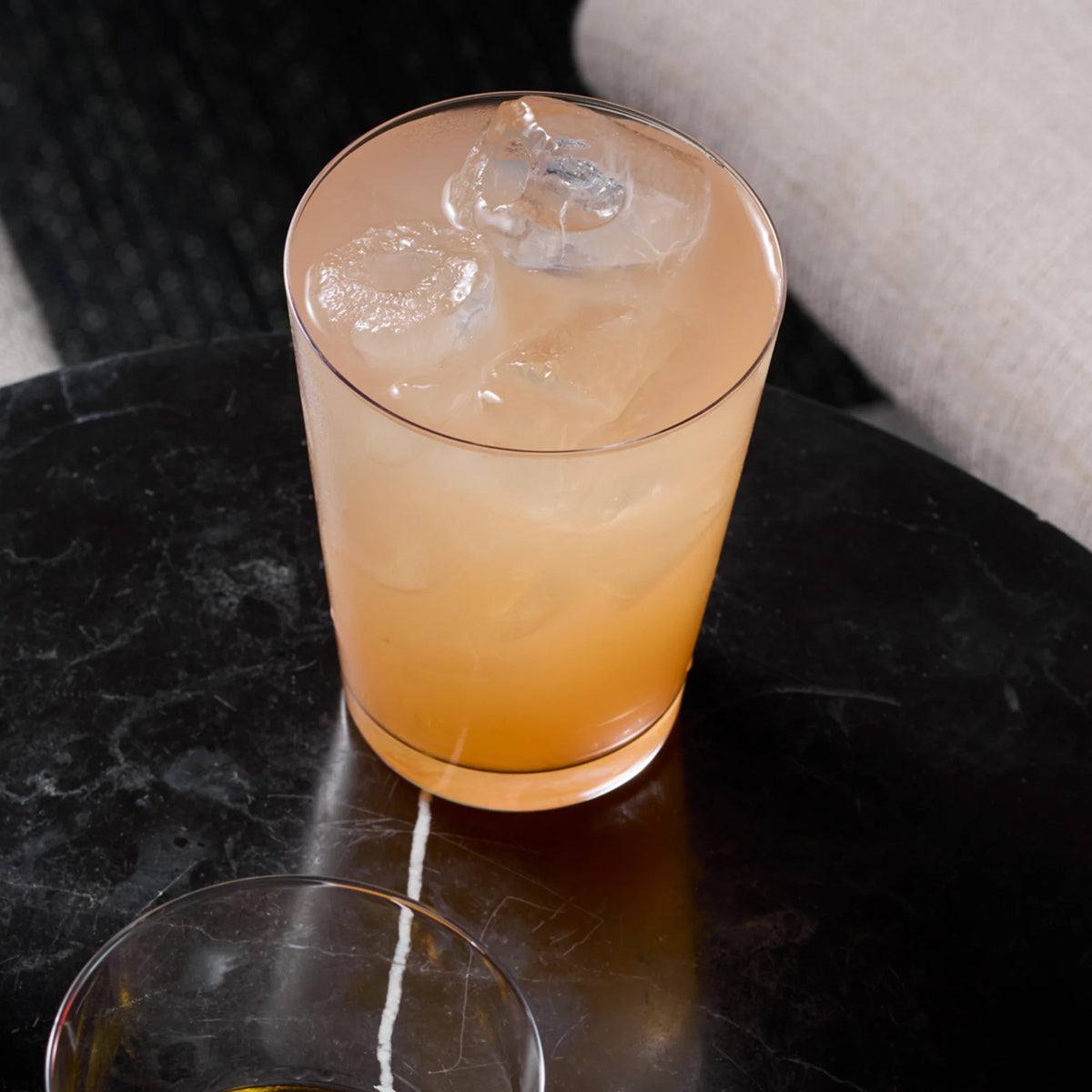 A clear Stölzle Metrico Medium Soft Drink / Long Drink Tumbler filled with a peach-colored drink and ice cubes sits on a dark stone table.