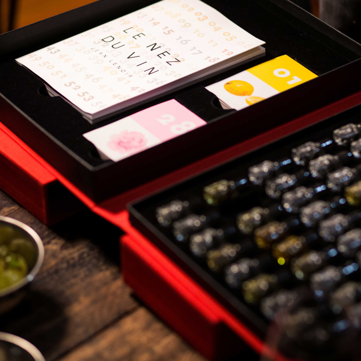 Wine bottles in a red box with cards on a wooden surface