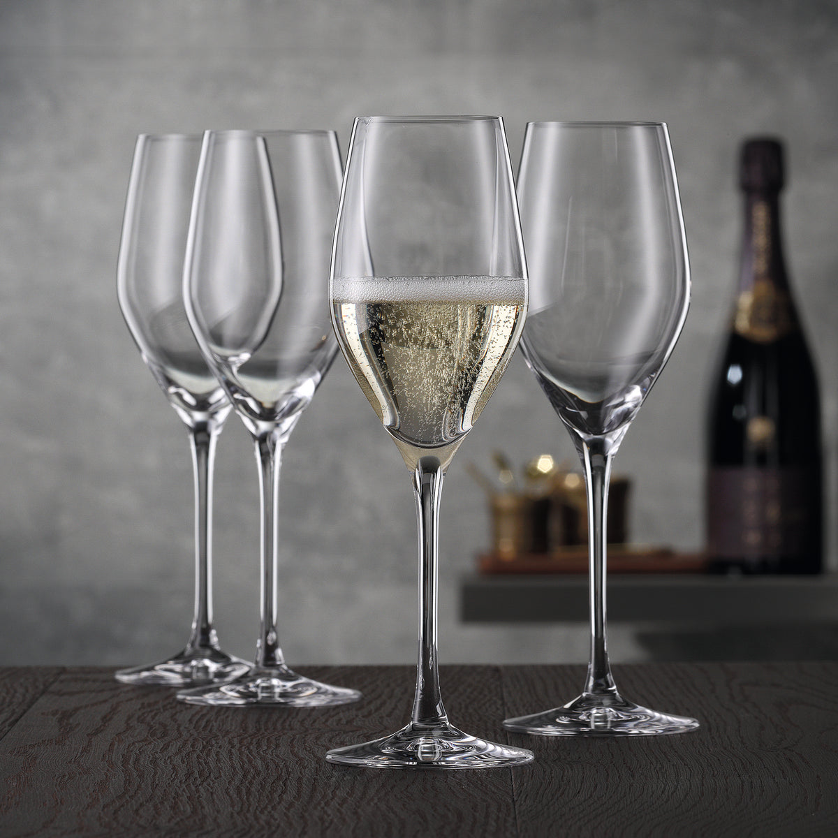 Four tall, slender Spiegelau Restaurant Authentis Champagne Glass 220ml - Set of 12 flutes stand on a wooden surface, with one glass filled with sparkling wine.