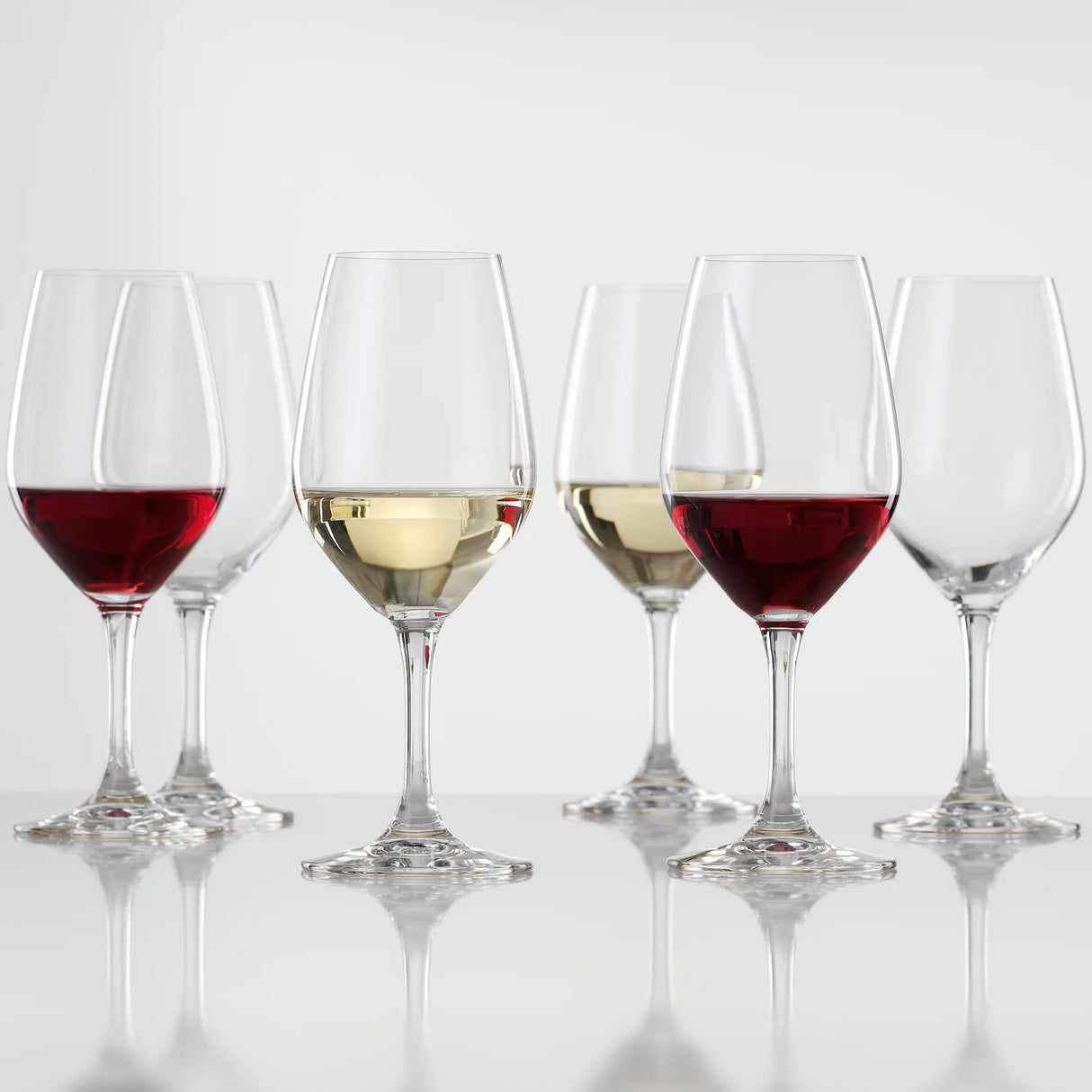 Six Spiegelau Expert Wine Tasting Glasses (260ml, set of 6) by Spiegelau are arranged in two neat rows; three glasses hold red or white wine while the other three remain empty. Each crystalline wine glass is displayed on a reflective surface with a plain white background, accentuating their clarity and elegance.