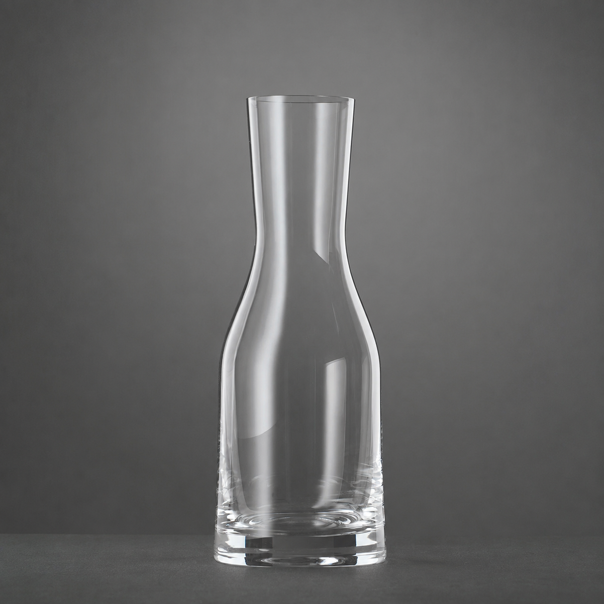 A clear, empty Spiegelau Ultra Wine / Water Carafe 500ml by Spiegelau stands upright on a dark surface against a plain gray background.
