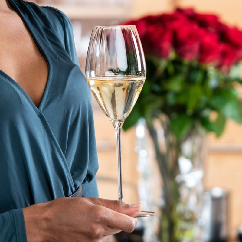 Person holding a glass of champagne with a blurred background of flowers and decor.