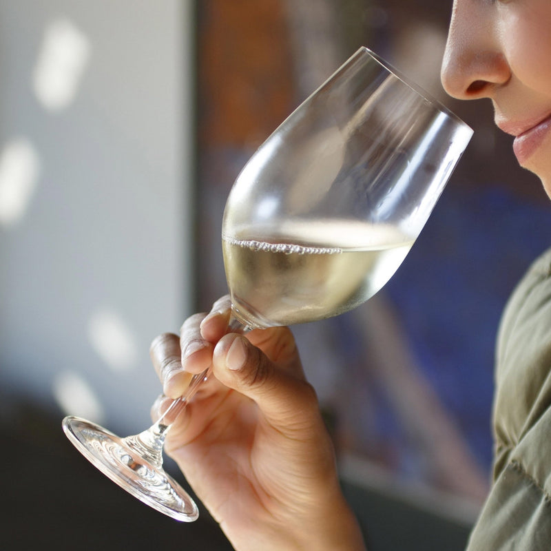 Person smelling white wine from a glass with a blurred background