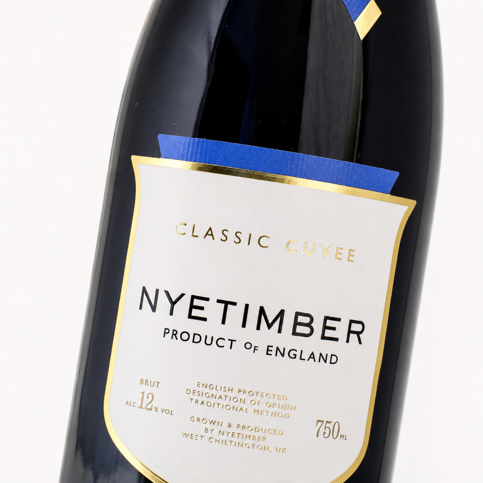 A close-up of a Nyetimber Classic Cuvee sparkling wine bottle label, showing product details including Product of England, Brut, 12% alcohol, and 750ml volume. The label has gold, white, and blue accents.