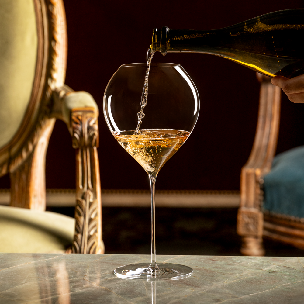 White wine being poured from a bottle into a mouth-blown Lehmann Glass La Poétique Grand Rouge Red Wine Glass 700ml on a stone table.
