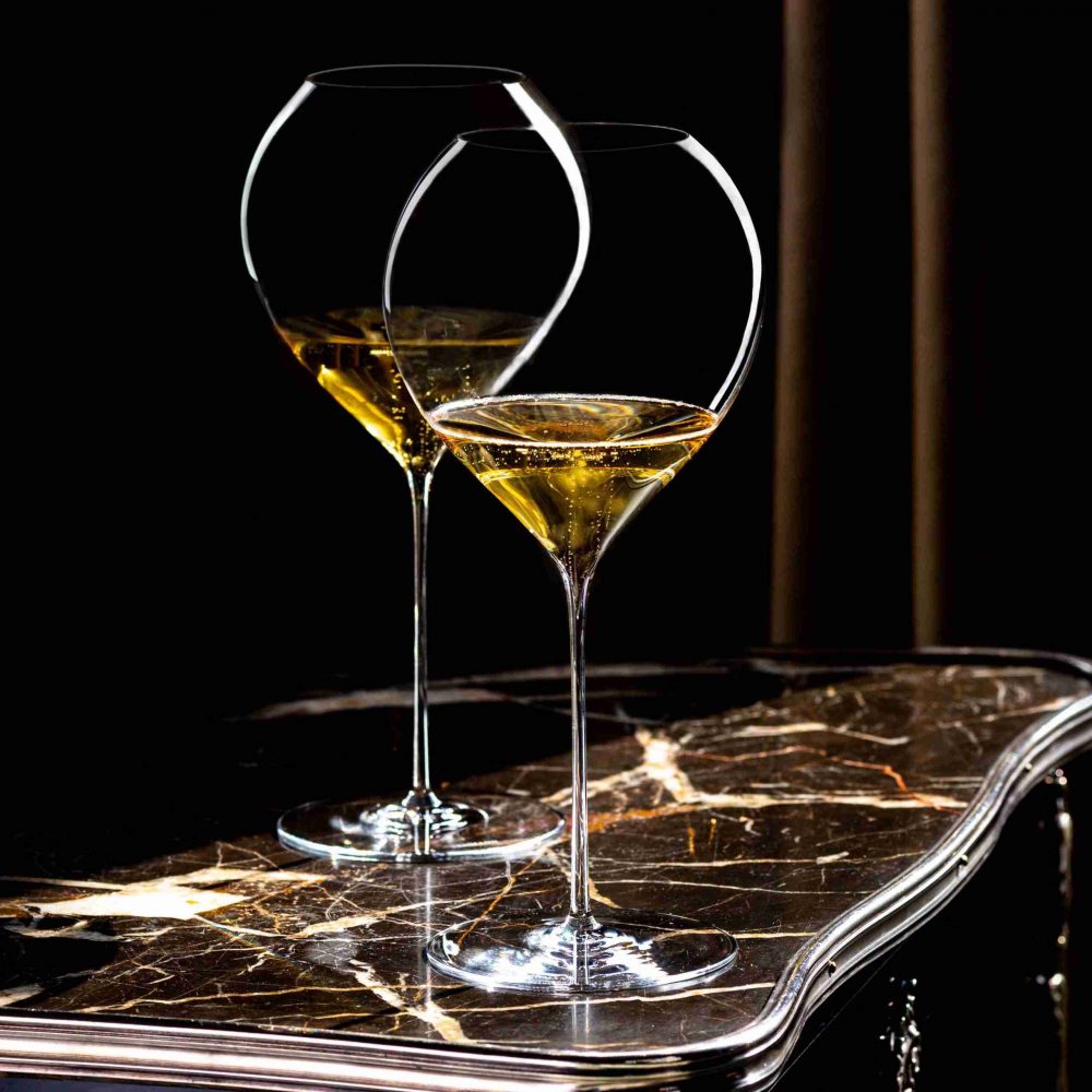 Two mouth-blown, long-stemmed Lehmann Glass La Poétique Grand Rouge Red Wine Glass 700ml - Set of 6 glasses filled with sparkling golden liquid sitting on a marble table.