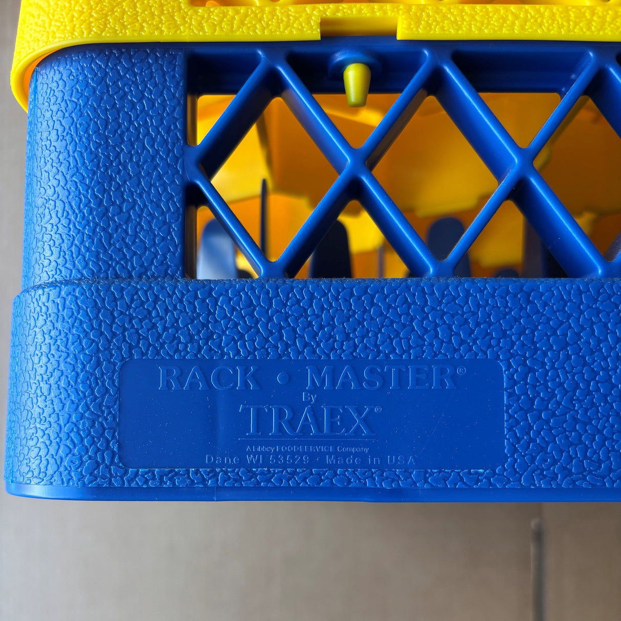 Close-up of a USED - GREAT CONDITION Traex Rack Master Glass Washer Tray (500 x 500 x 120mm, 30 glass capacity, 81mm cell) by Wineware. Blue and yellow plastic with embossed details; interior section is partially visible.