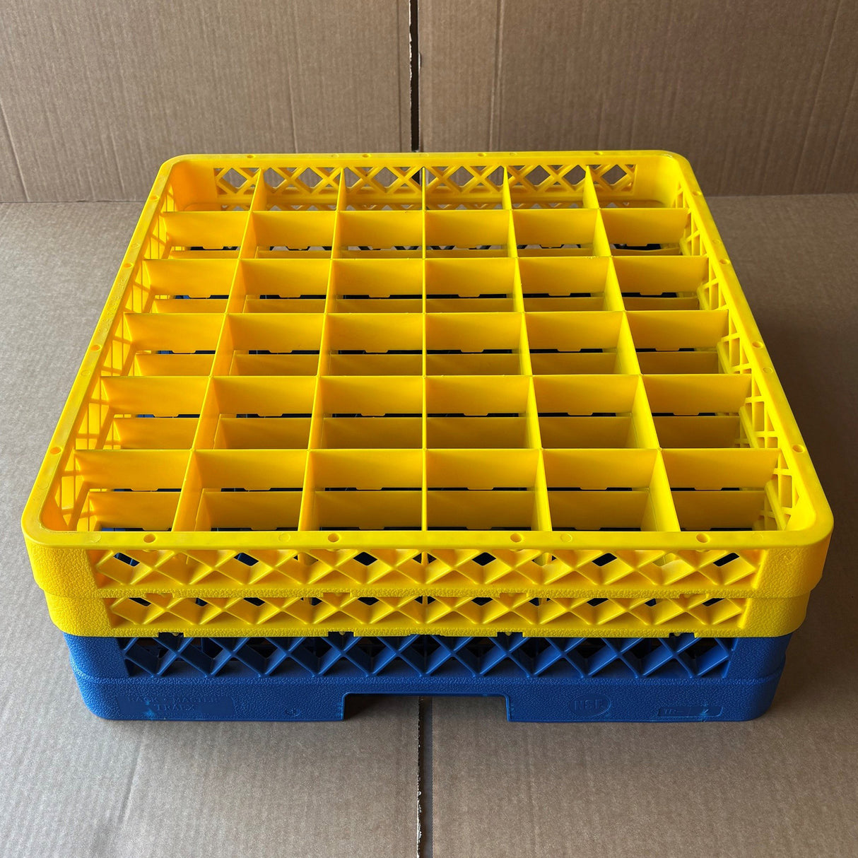 A Wineware Traex Rack Master Glass Washer Tray (500x500x160mm, 36 glasses, 75mm cell) in yellow plastic is stacked on a blue rack, both resting on cardboard.