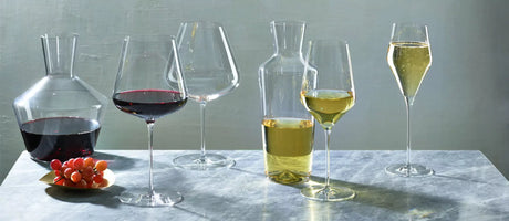 A collection of Zalto wine glasses for red and white wine, as well as a decanter and carafe, all sat on a marble table.