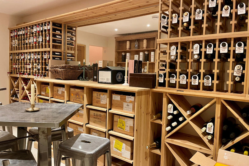 Wine cellar with bottles on wooden shelves and tables with stools.