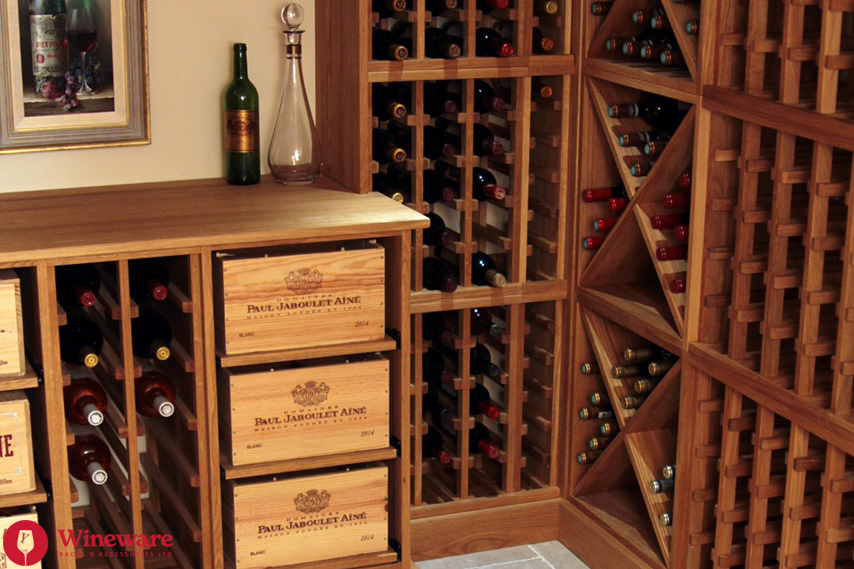 Wooden wine cellar with shelves and drawers filled with wine bottles.