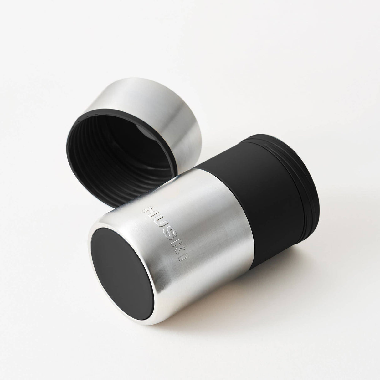 The Huski Wine & Champagne Bottle Cooler - Brushed Stainless Steel by Huski is displayed on a white background with its lid off and placed beside it. Featuring a black silicone grip, this insulated stainless steel cooler is perfect for keeping your wine or champagne at the ideal temperature.