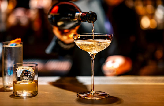 Bar scene with a bartender pouring a drink into a glass on a wooden bar.