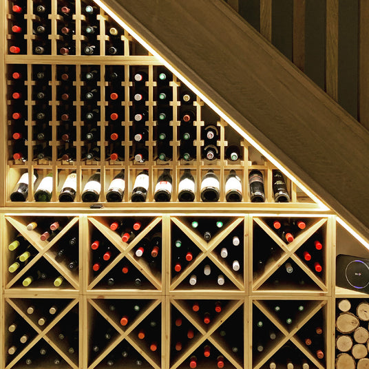 Wine bottles arranged in a wooden wine rack placed under stairs.