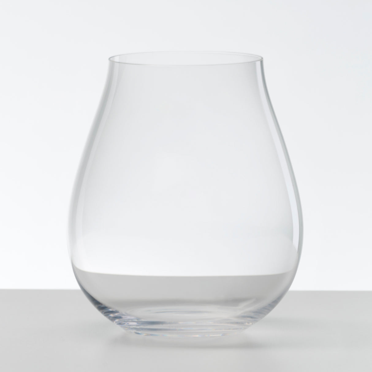 Two Riedel O Range Stemless New World Pinot Noir glasses (Set of 2 - 0414/67) sit elegantly on a white surface against a plain white background. With their wide, rounded base and gently narrowing silhouette, these clear glass pieces reflect the refined design Riedel is known for. Dishwasher friendly and stylishly understated, they complement any setting with ease.