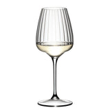 A Riedel Restaurant Grape Optical White Wine / Champagne / Spritz Glass (590ml) from Riedel, made from lead-free crystal and featuring vertical optical lines, is half-filled with white wine and stands against a plain white background.