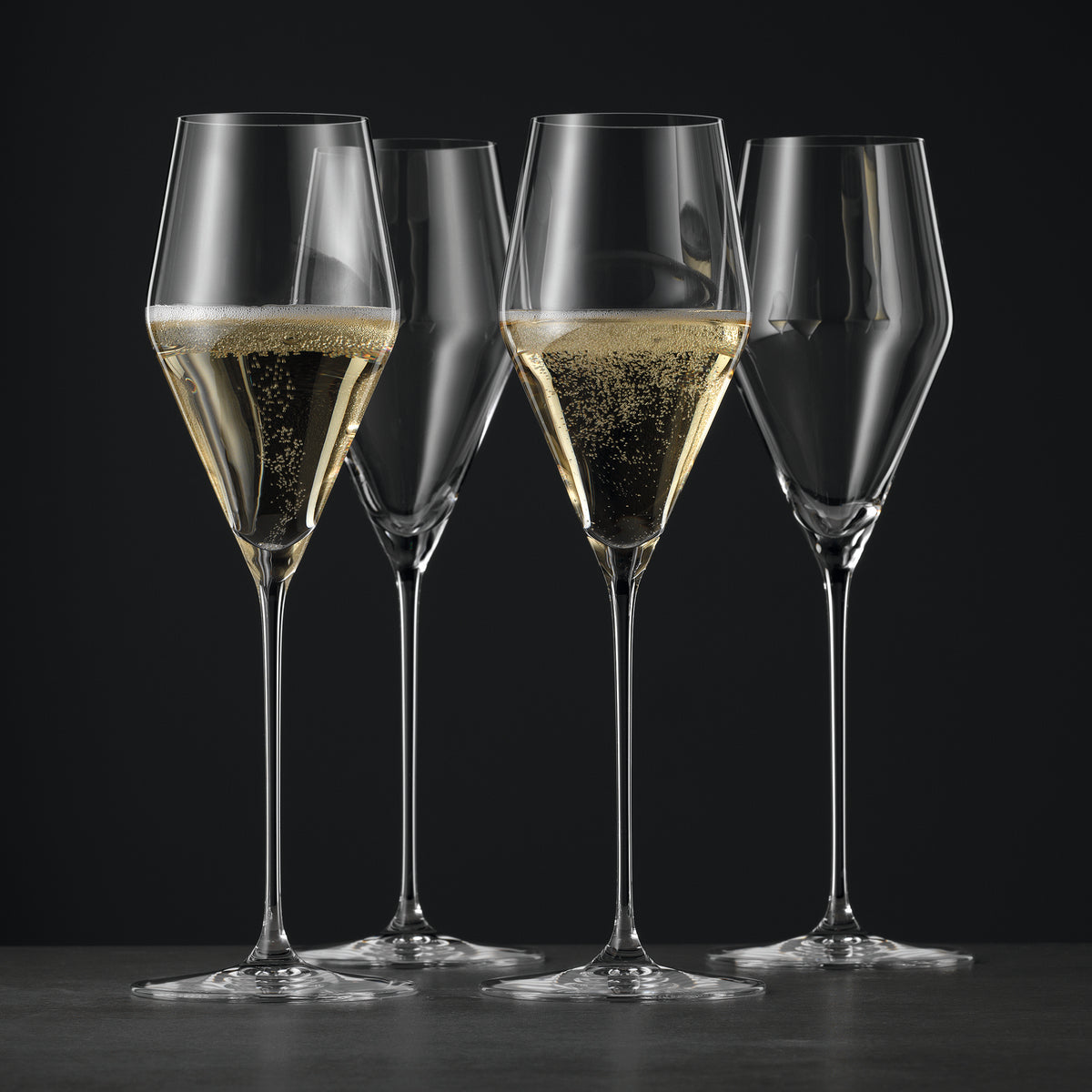 Four elegant Spiegelau Definition Universal Red & White Wine Glasses—crafted from fine crystal glass—stand gracefully, two filled with wine and catching the light, two empty, all set against a dark background on a smooth surface.