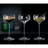 Three elegant, long-stemmed coupe glasses from the Spiegelau Hi-Lite Coupette / Cocktail Saucer - Set of 2 by Spiegelau are displayed side by side. The left glass features a dark drink with a frothy top, the center glass is empty, and the right Spiegelau Hi-Lite holds a light cocktail garnished with an olive on a stick.