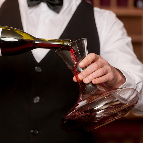 A person in formal attire pours red wine into a Stölzle Classic Mouth-Blown Red Wine Decanter 750ml, carefully holding the handmade crystal decanter to aerate the wine.
