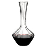 A Riedel Manufaktur Exquisit Wine Decanter 1.2L by Riedel, featuring a wide base that narrows at the neck, is partially filled with red wine.