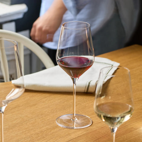 Three Stölzle STARlight Red Wine Glass units on a wooden table, with one glass filled with red wine and another filled with white wine.