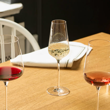 A tall, tapered Stölzle STARlight Champagne / Sparkling Wine Glass filled with sparkling wine, centered between two Stolzle STARlight crystal wine glasses containing red and rosé wine on a wooden table.