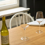 Two clear Stölzle STARlight Bordeaux Red Wine Glass - Set of 6 glasses stand on a wooden table next to a bottle of white wine.