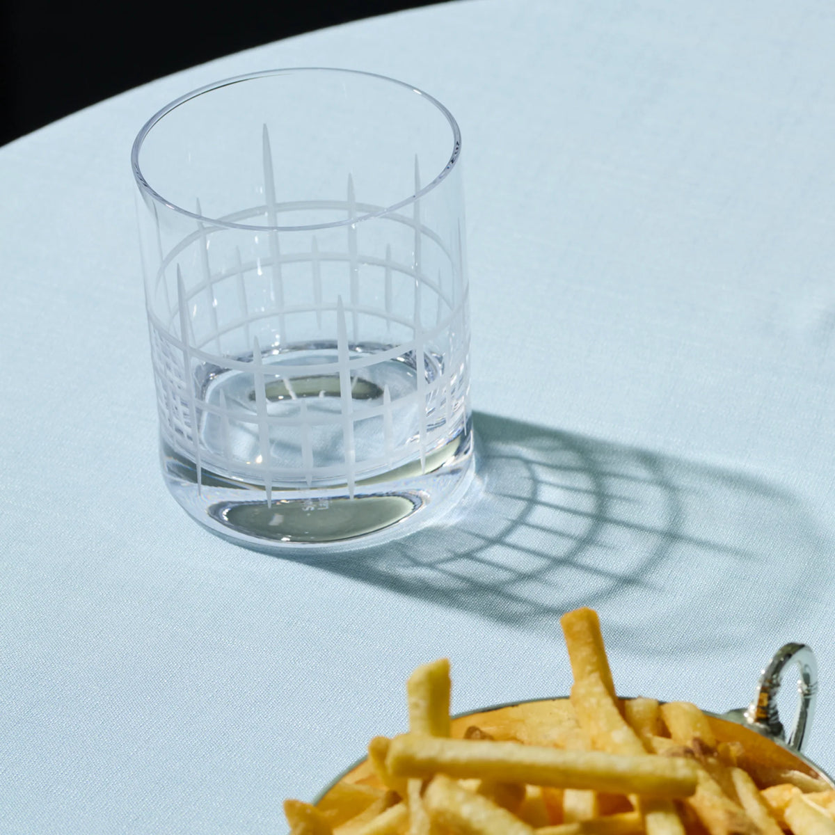 Empty Stölzle Manhattan Bar Whisky Tumbler 320ml - Set of 6 with a white etched grid pattern on a light blue tablecloth next to a bowl of french fries.