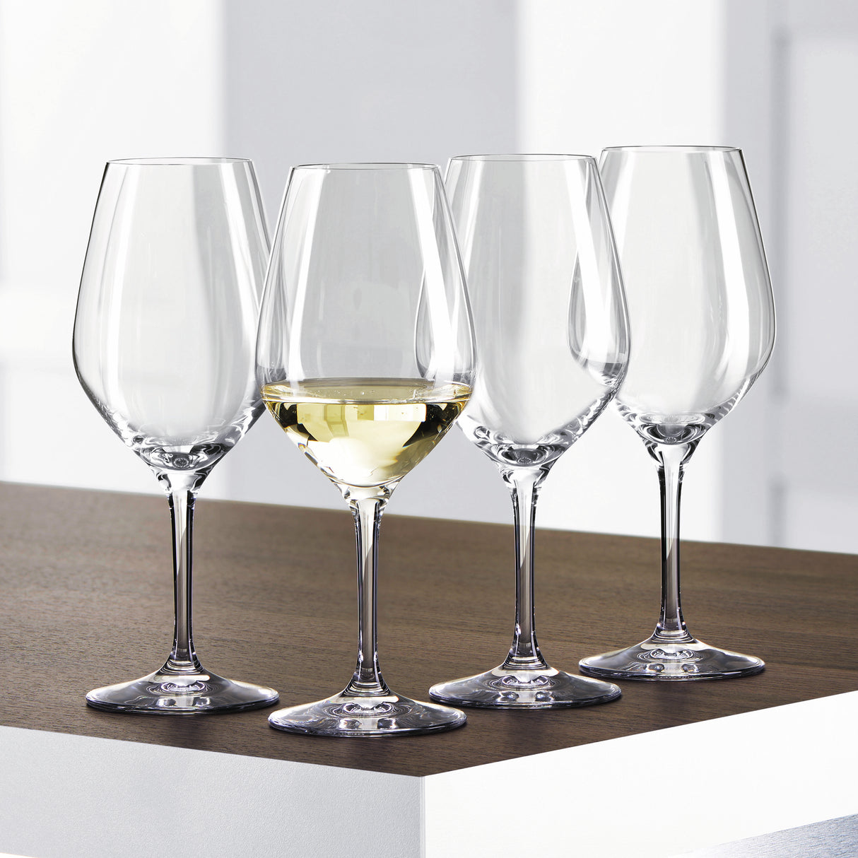 Twelve Spiegelau Restaurant Authentis Small White Wine Glasses by Spiegelau, each with a 360ml capacity, are arranged on a wooden and white surface; three glasses remain empty while one is filled with white wine, showcasing the professional crystal design's elegance and craftsmanship.