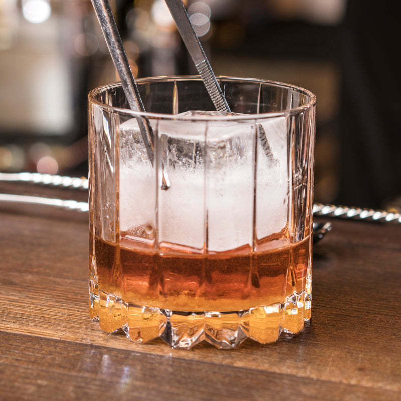 Close up image of a Riedel whisky glass with a lump of ice being added with tongs.