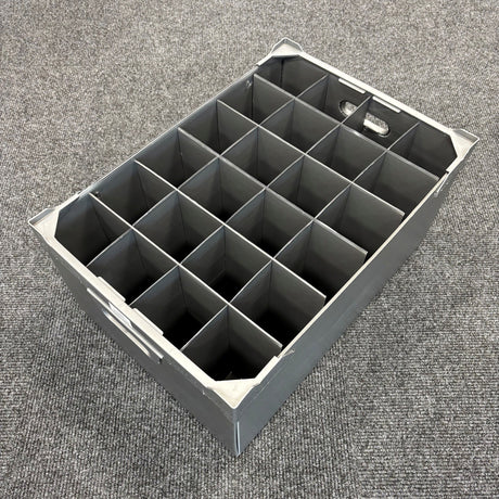 A USED - GREAT CONDITION Wine Glass Storage Box by Wineware, featuring 24 square compartments and measuring 230mm high, sits empty on a gray carpeted floor. The gray plastic box has handles on both ends and is ideal for securely storing wine glasses.