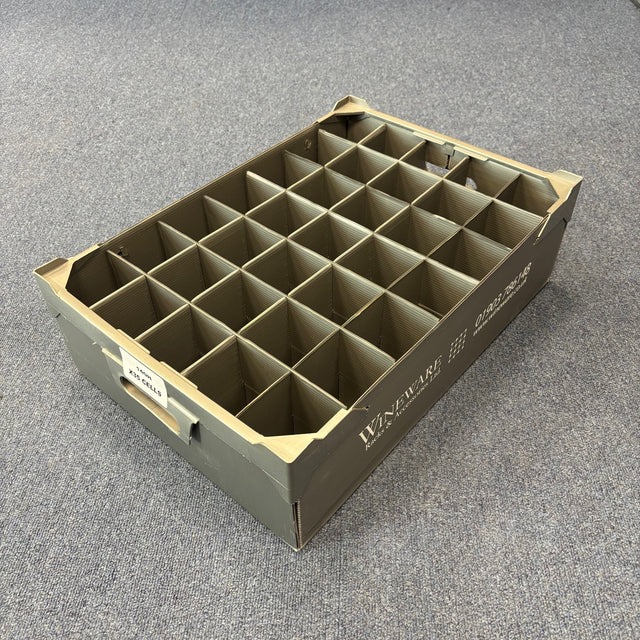 The Wineware USED - GREAT CONDITION Wine Glass Storage Box (140mm High, 35 Cells) is a gray plastic organizer with square grid compartments and labels on the front and side, shown on a blue-gray carpeted floor.