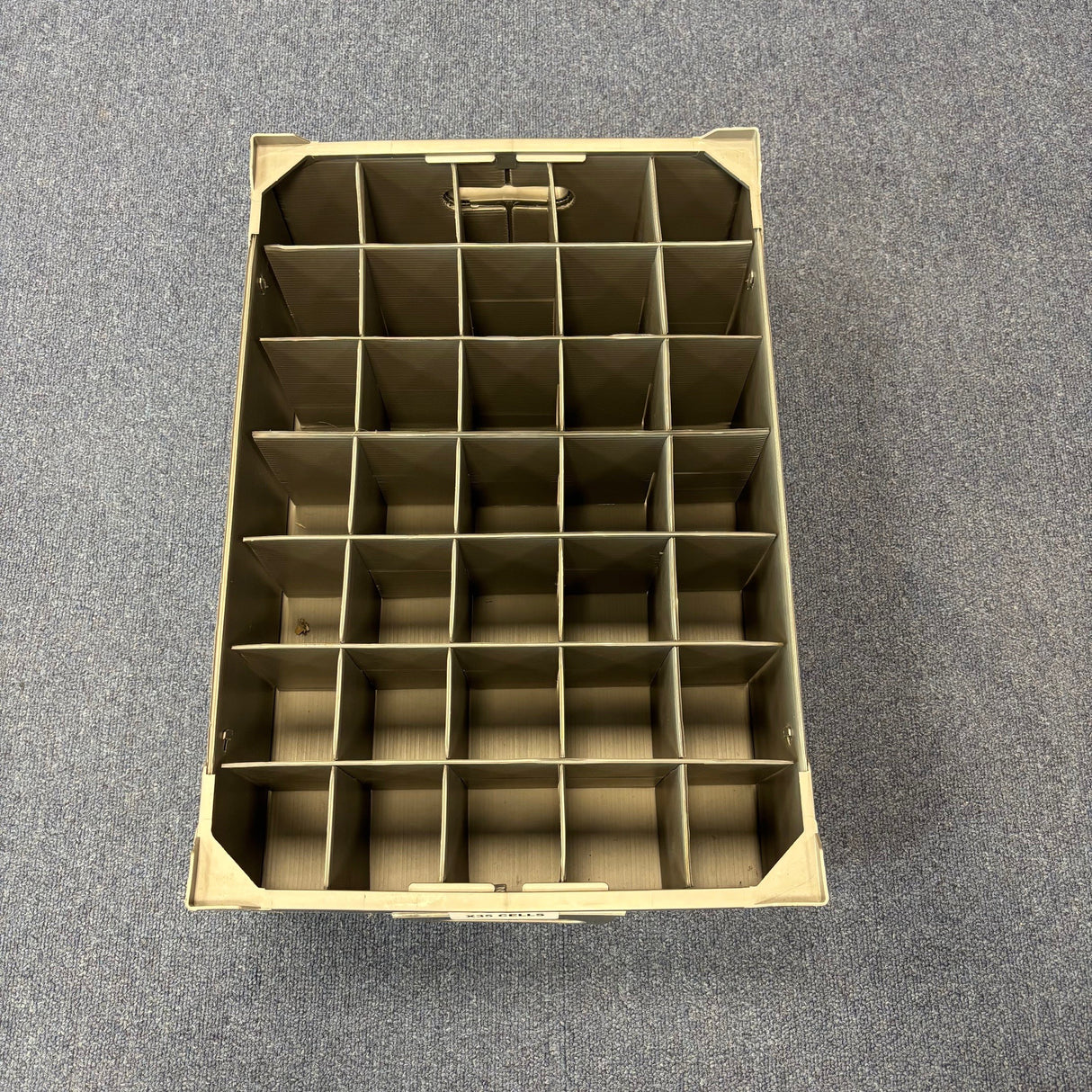 A Wineware USED - GREAT CONDITION Wine Glass Storage Box, beige with 35 compartments and 140mm height, is shown on a grey carpeted floor, viewed from above.