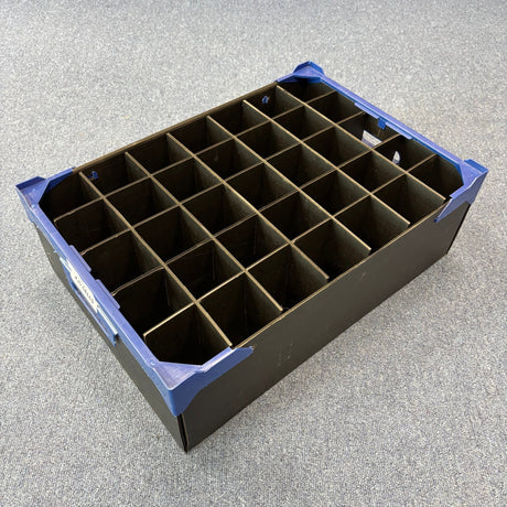 A USED - GREAT CONDITION Wineware Wine Glass Storage Box, 160mm high with 35 cells, made of black plastic with blue corners and internal dividers, sits on a grey carpeted floor—perfect for organizing wine glasses or glassware.