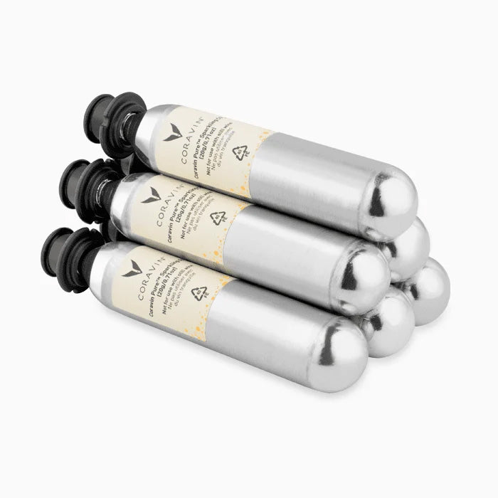 Six cylindrical silver Coravin Pure Sparkling Wine CO2 Capsules stacked in a pyramid formation with black caps.