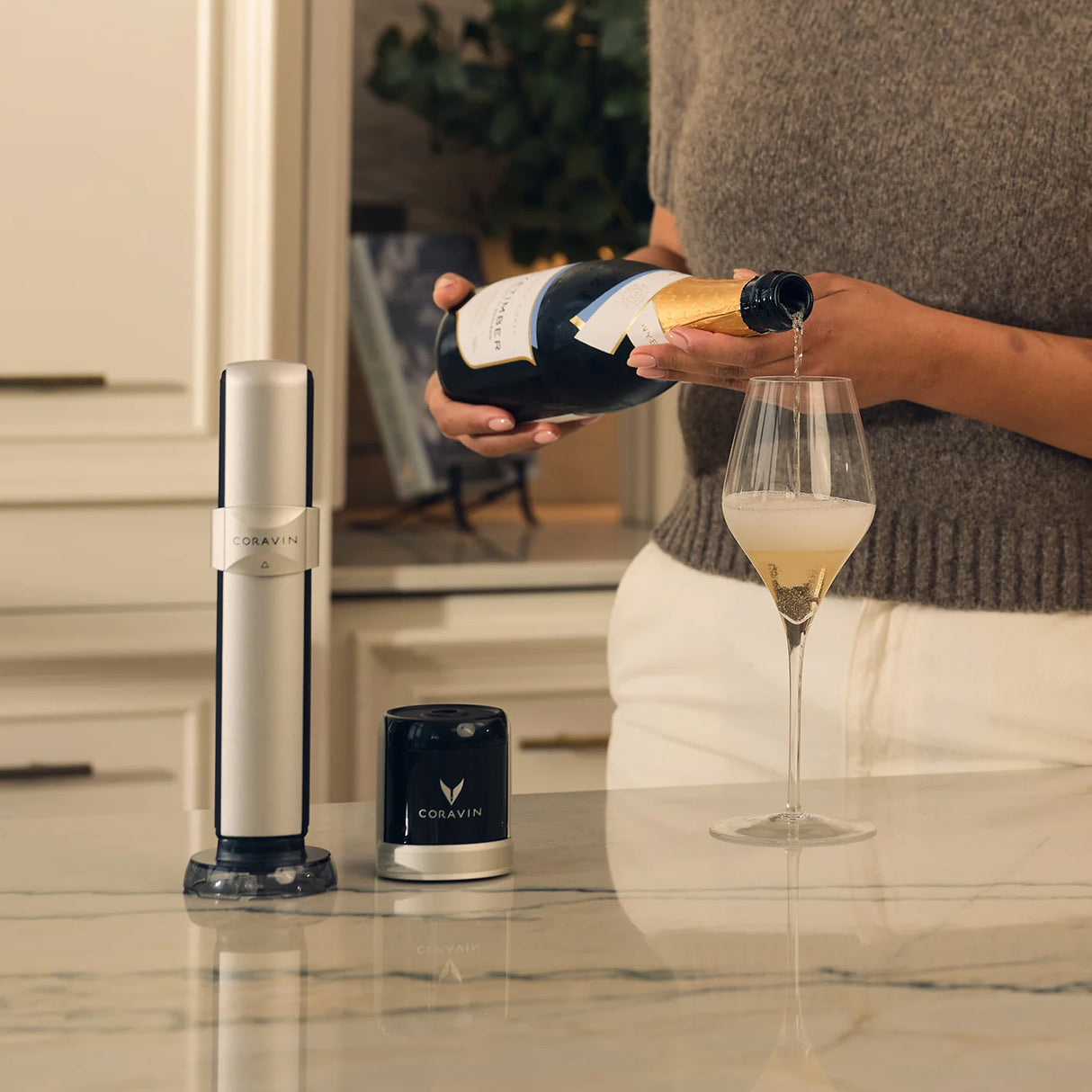 A person pours sparkling wine into a glass on the kitchen counter, with the Coravin Sparkling Wine Preservation System by Coravin, its components, and CO2 capsules nearby—perfect for keeping sparkling wine at its best.