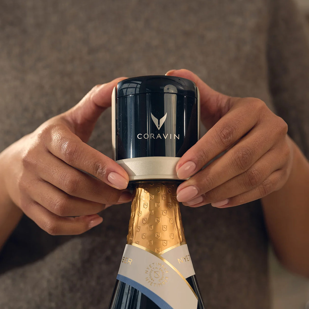 A person holds a Coravin Sparkling Wine Stopper from the Coravin Sparkling Wine Stopper - Set of 2, placing it onto the top of a sealed champagne bottle wrapped in gold foil—a perfect demonstration of using Coravin’s preservation system designed specifically for sparkling wine bottles.
