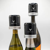 Three sparkling wine bottles, each sealed with a black and silver Coravin Sparkling Wine Stopper from the Coravin Sparkling Wine Stopper - Set of 2, are displayed against a plain white background.