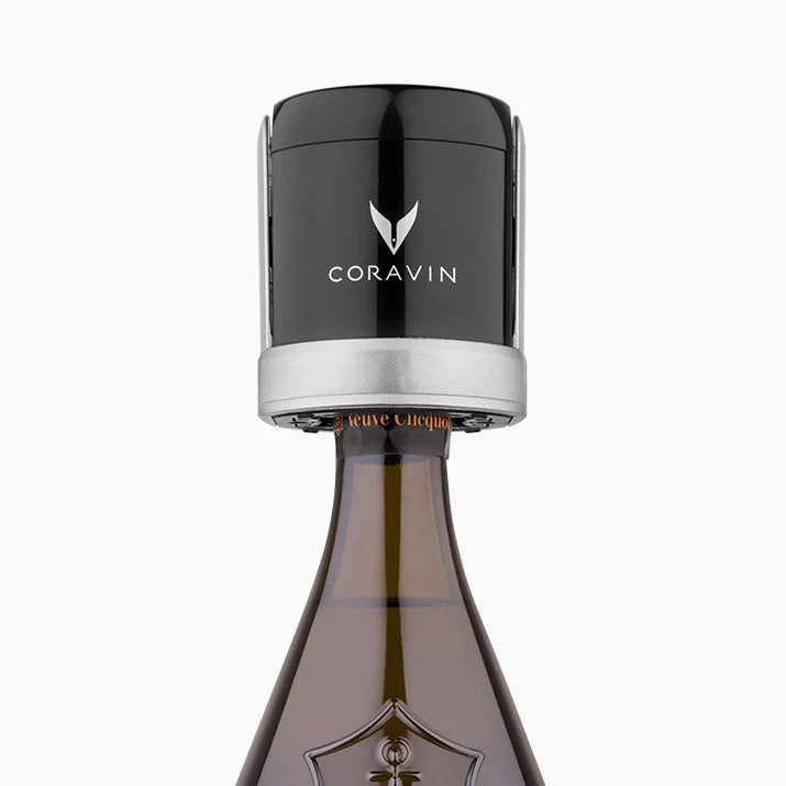 A set of two black and silver Coravin Sparkling Wine Stoppers by Coravin is shown attached to the neck of a champagne bottle, illustrating the innovative sparkling wine preservation solution against a plain white background.