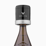 A set of two black and silver Coravin Sparkling Wine Stoppers by Coravin is shown attached to the neck of a champagne bottle, illustrating the innovative sparkling wine preservation solution against a plain white background.