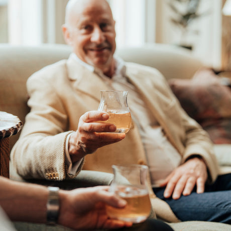 Man sitting on a couch holding a glass of whisky, smiling.