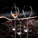 A bottle pours sparkling wine into a Lehmann Glass Jamesse Grand Champagne 300ml glass from the set of 6, with two empty crystal glasses nearby on a polished dark marble table against a blurred black background.