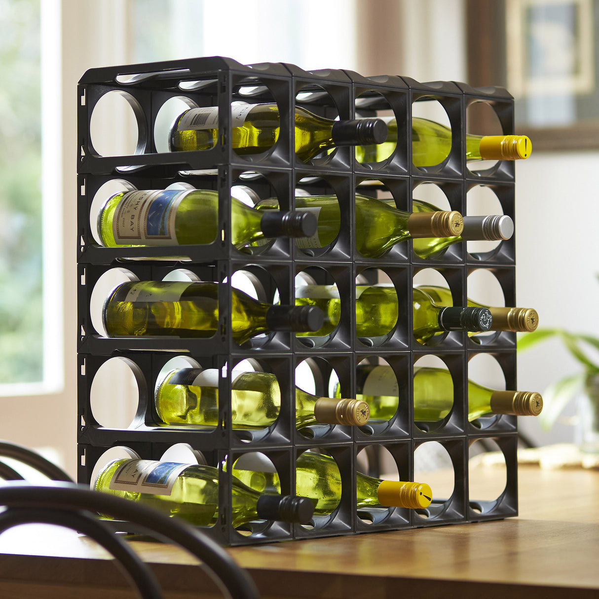 The Stakrax 30 Bottle Plastic Wine Rack - Black by Stakrax holds multiple bottles horizontally, offering expandable wine storage—perfect for a modern, well-lit room.