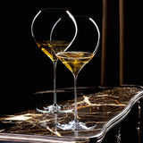 Two mouth-blown, long-stemmed Lehmann Glass La Poétique Grand Rouge Red Wine Glass 700ml - Set of 6 glasses filled with sparkling golden liquid sitting on a marble table.
