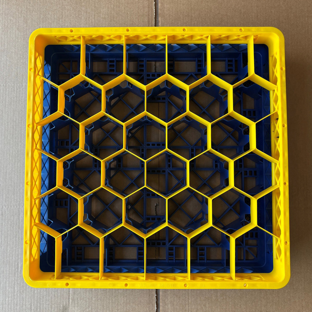 A USED - GREAT CONDITION Wineware Traex Rack Master Glass Washer Tray (500x500x120mm, 30 glasses, 81mm cell), featuring a yellow and blue hexagonal grid, sits on cardboard and is viewed from above.