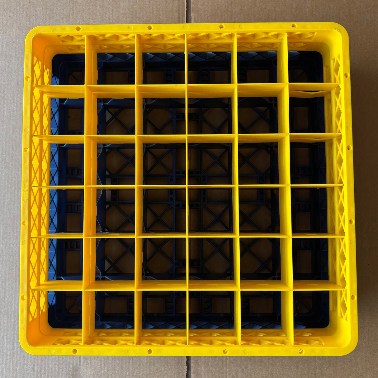 A top-down view of a yellow Wineware Traex Rack Master Glass Washer Tray (500x500x160mm, 36 glasses, 75mm cell) in great used condition is placed on a black glasswasher rack against a brown cardboard background.